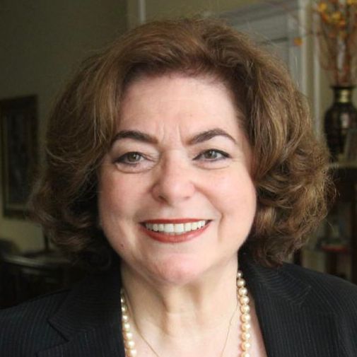 Smiling woman with curly hair and pearls.